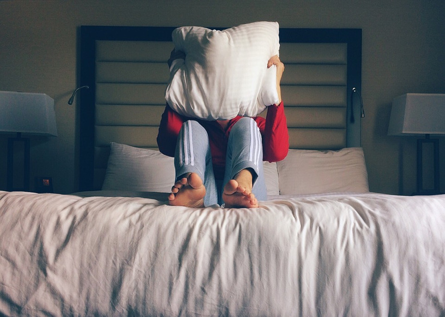 mężczyzna na łóżku, zakrywający się poduszką