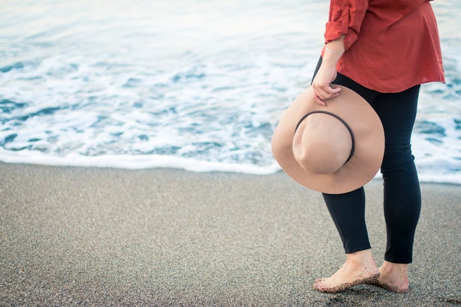 kobieta na plaży z kapeluszem w ręce