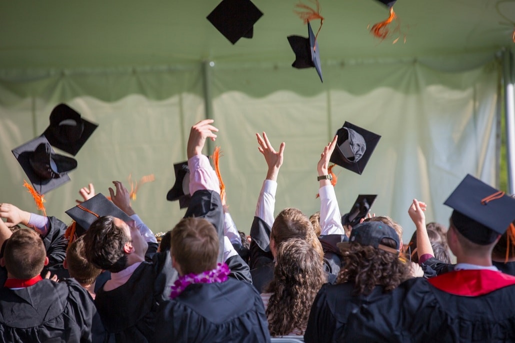 Absolwenci-studenci rzucają czapkami na koniec studiów