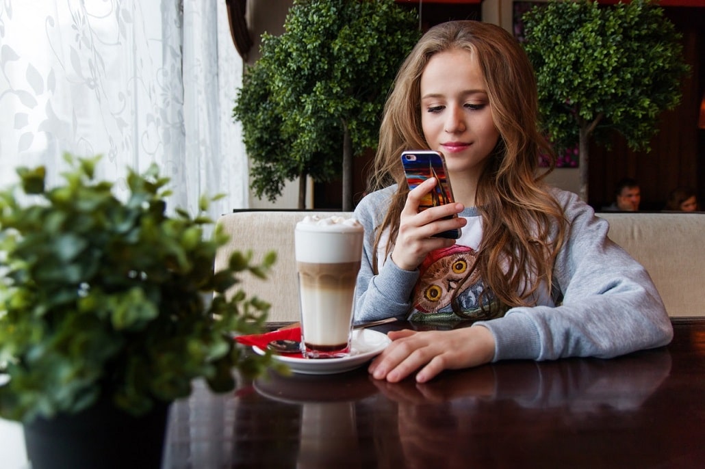Młoda dziewczyna na kawie, wpatrzona w swój telefon