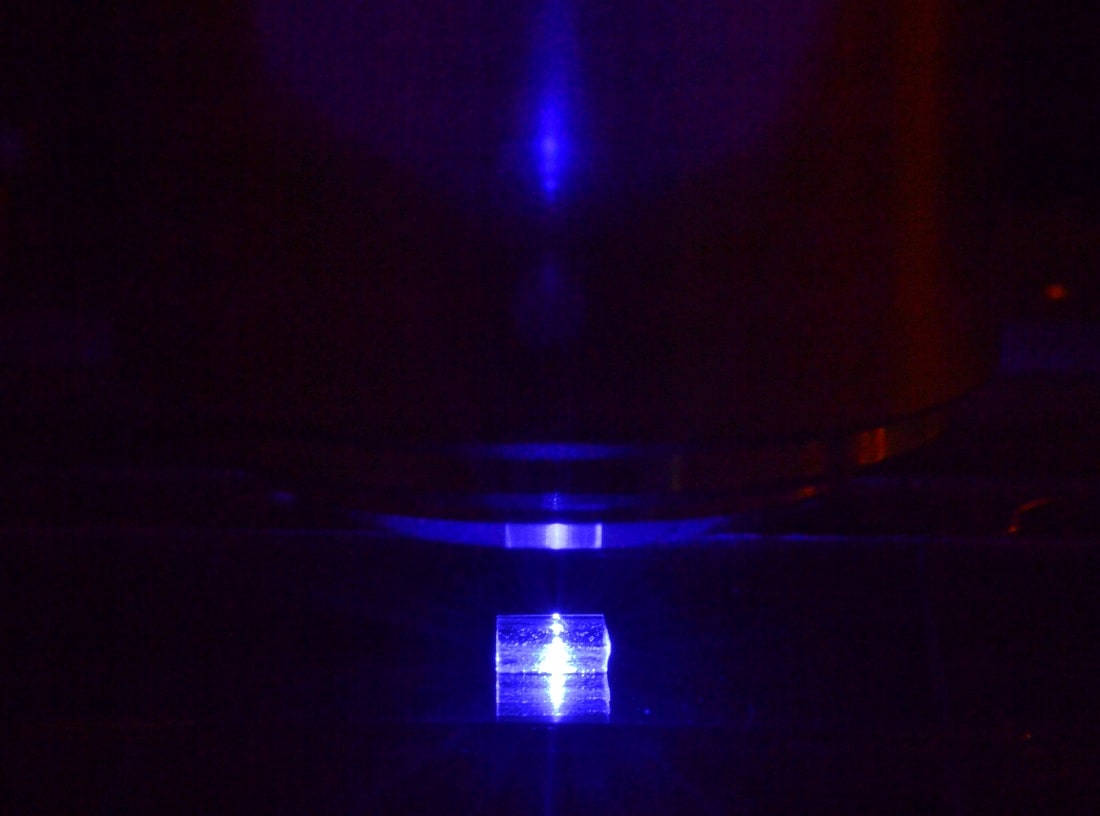 Kryształ fluorku litu z zarejestrowanymi śladami ciężkich jonów podczas oglądania pod mikroskopem fluorescencyjnym