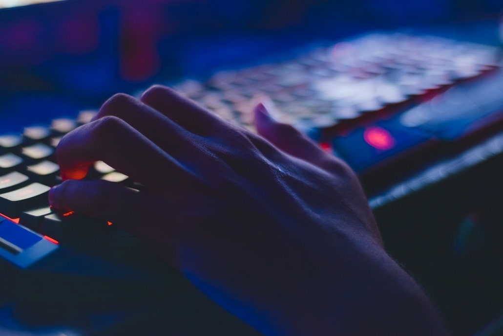 Dłoń na podświetlanej klawiaturze, symboliczne ukazanie grania w gry komputerowe